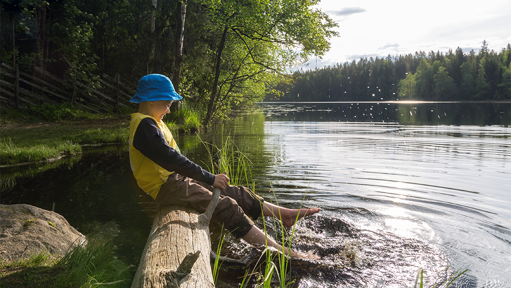 En pojke sitter vid en sjö i Finland och skvätter vatten med fötterna. Han lever i värdens lyckligaste land, enligt en ny FN-rapport