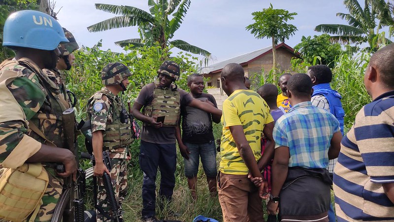 Soldater i och civila samtalat framför ett hus och en palm.