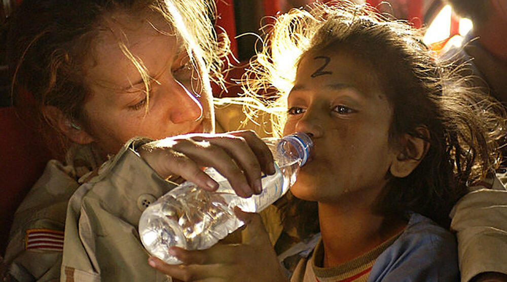 Kvinnlig biståndsarbetare ger afghansk flicka vatten att dricka ur flaska