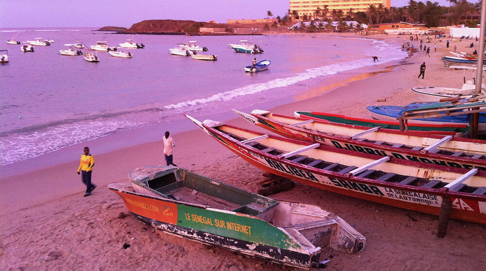 En strand i Senegals huvudstad Dakar i solnedgång med båtar.