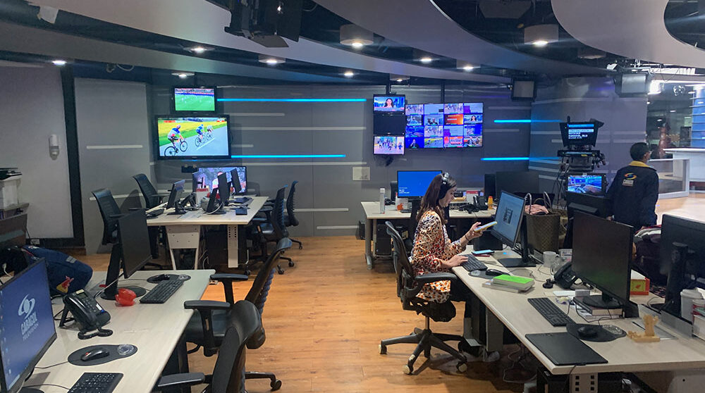 En tv-station i colombia, skärmaroch en reporter vid ett skrivbord