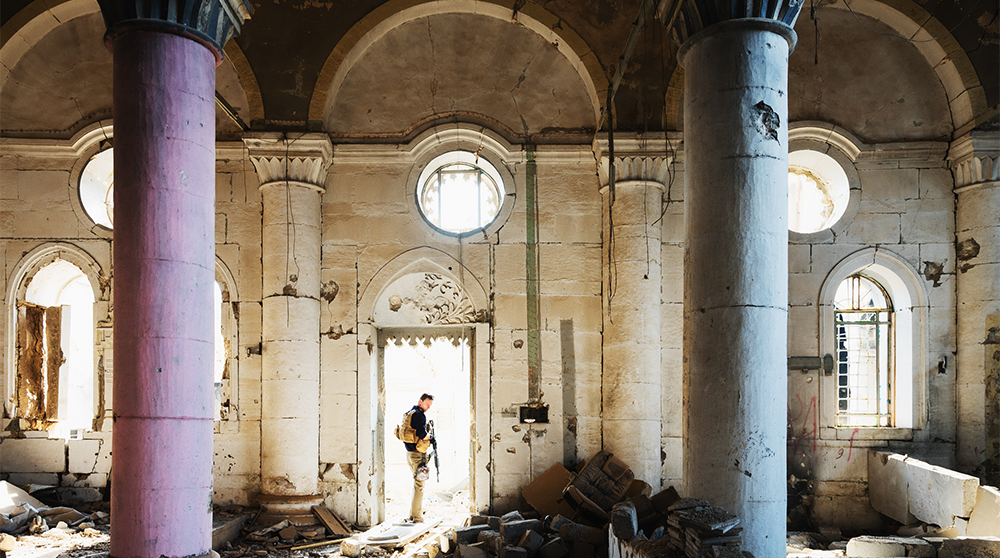 Mosul, Irak, den 21 november 2018. En okänd säkerhetsentreprenör står i dörröppningen till ruinerna av en kyrka som förstördes i striderna mot ISIS. Foto: Shutterstock